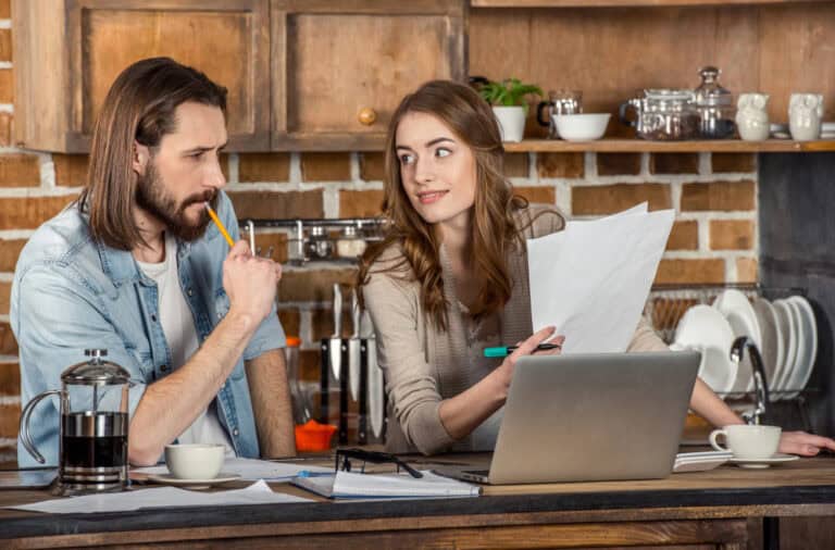 Thoughtful couple discussing architectural plans at kitchen counter.